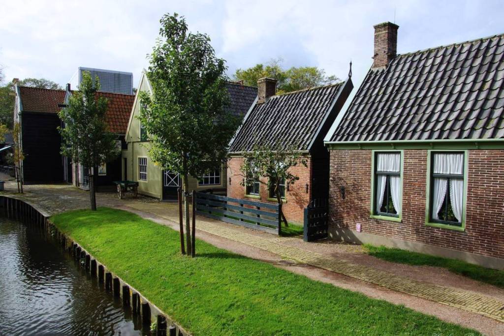 Eine Reihe historischer Häuschen steht entlang eines schmalen Kanals mit grünen Ufern im Zuiderzeemuseum in Enkhuizen.