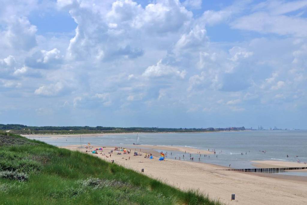 Breed zandstrand bij badplaats Cadzand-Bad met recreanten en groene duinen langs de Zeeuwse kustlijn.