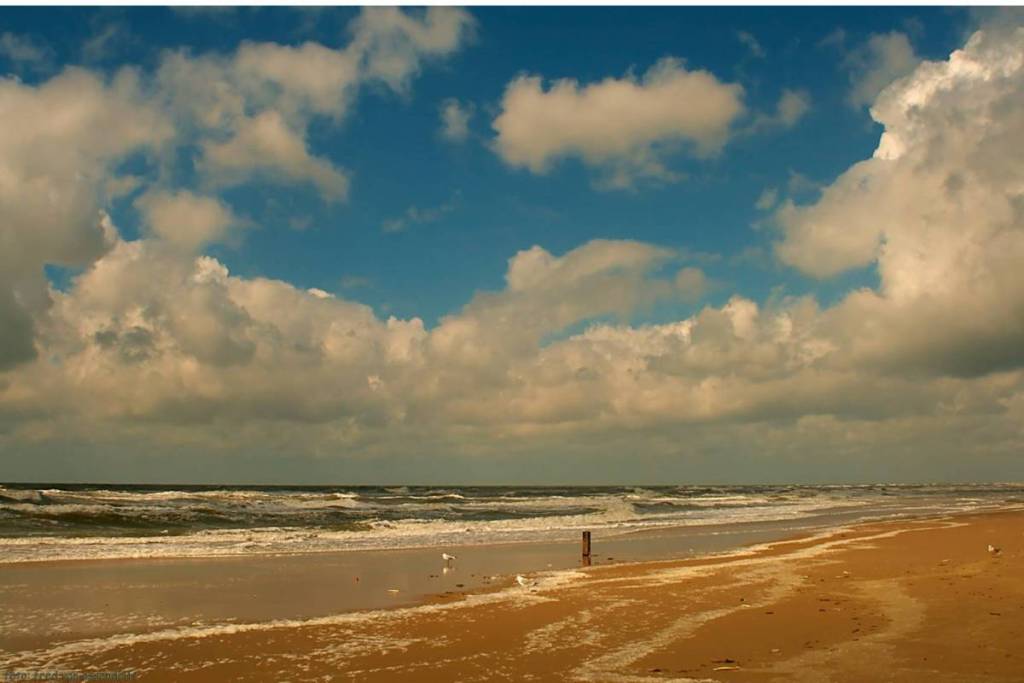 uig Noordzeestrand bij Callantsoog met rollende golven onder een indrukwekkende, bewolkte lucht.