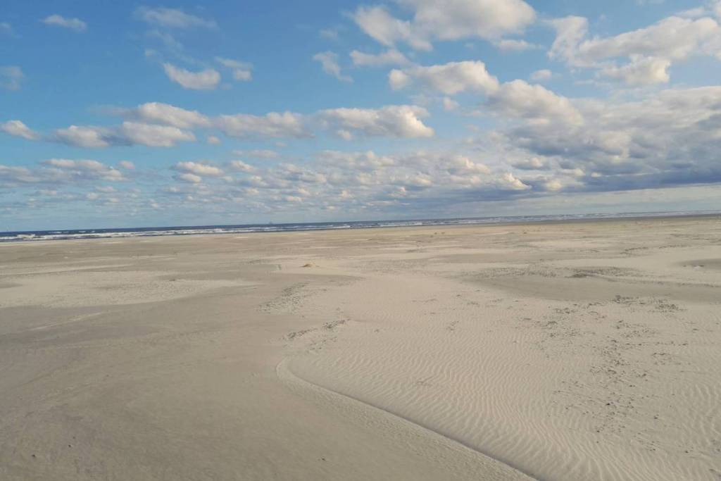 Het extreem brede en verlaten Oosterstrand op Schiermonnikoog onder een lichtbewolkte blauwe hemel.