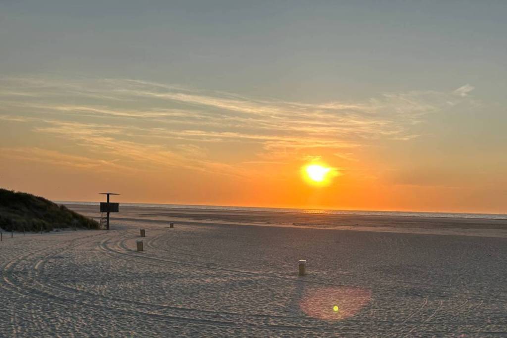 Sfeervolle zonsondergang over het brede Noordzeestrand van Ouddorp met een houten strandwachtpost aan de duinrand.