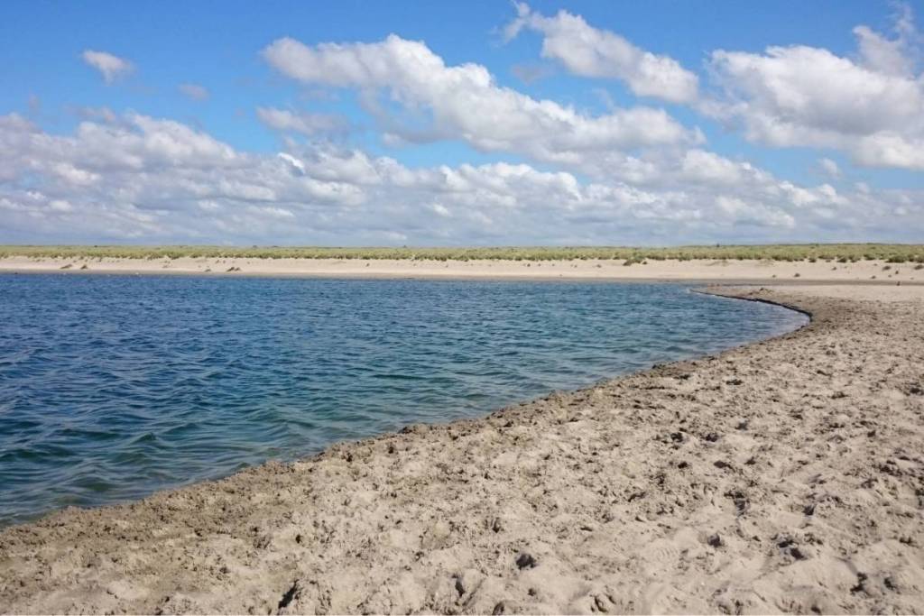 Een kalme getijdenpoel op de Zandmotor bij Monster omringd door een brede, dynamische zandvlakte.