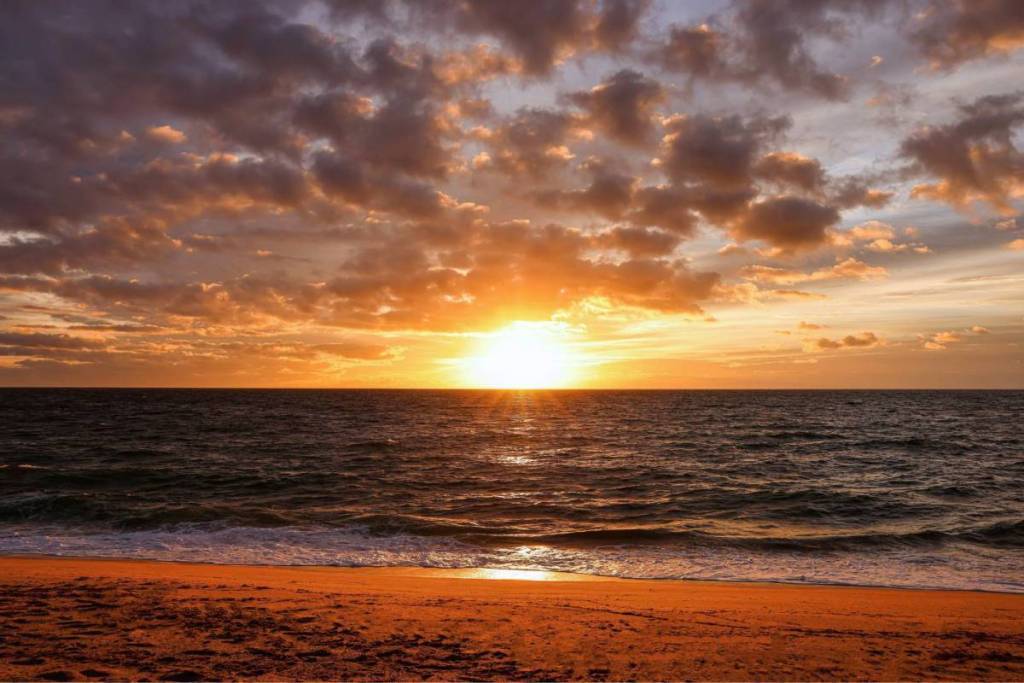 Een kleurrijke zonsondergang boven de kalme Noordzee vanaf een goudgeel zandstrand in Nederland met een dramatisch wolkendek.