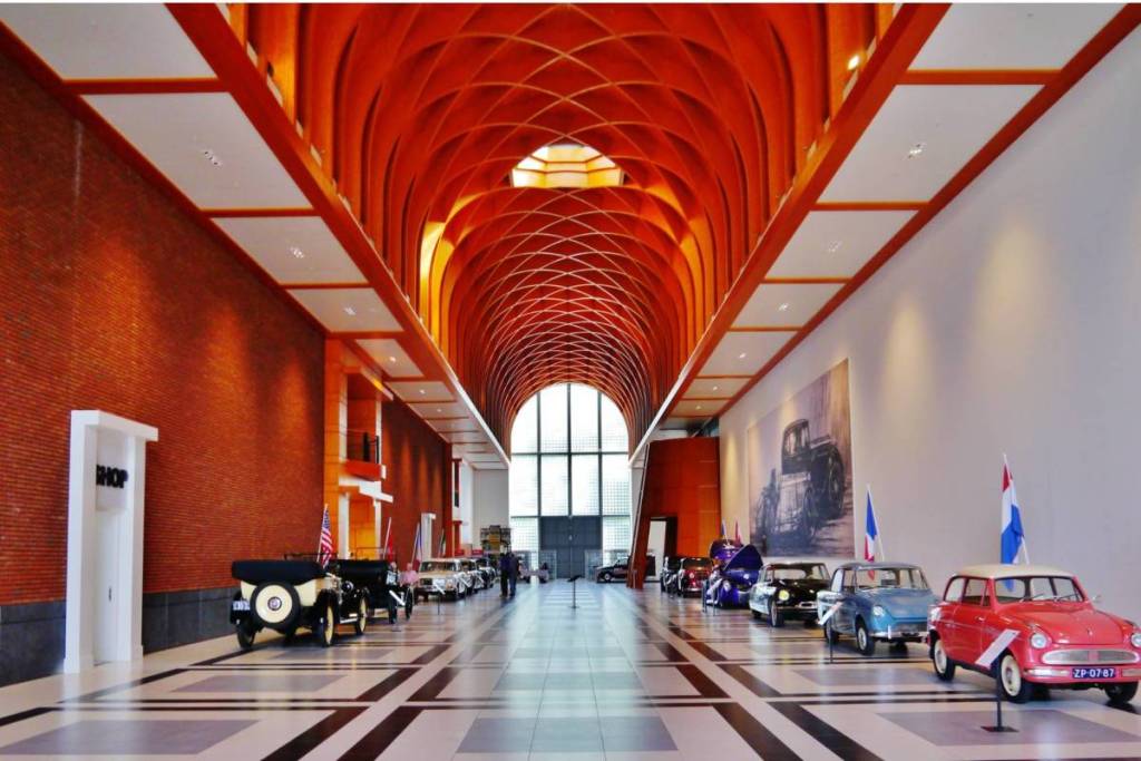 Die monumentale zentrale Halle des Louwman-Museums in Den Haag, mit einem beeindruckend hohen hölzernen Gewölbe und historischen Oldtimern entlang der Wände.