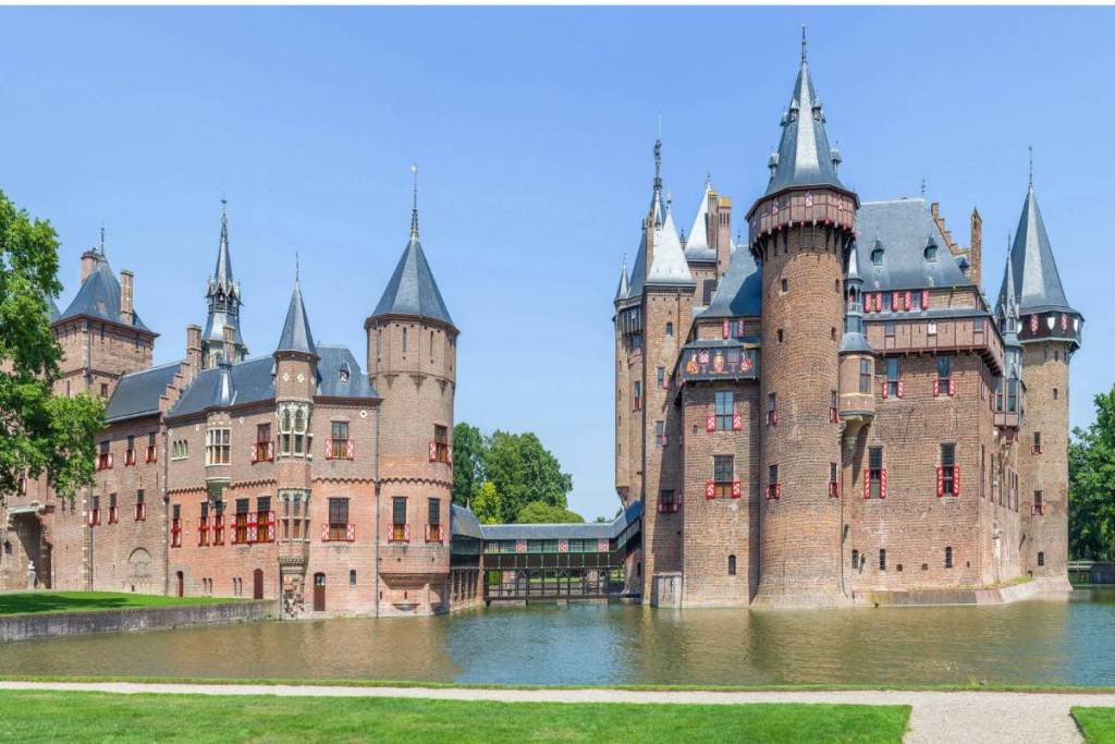 Vista lateral del castillo de Haar reflejado en el foso, con el emblemático puente cubierto que lo une, en un día soleado.
