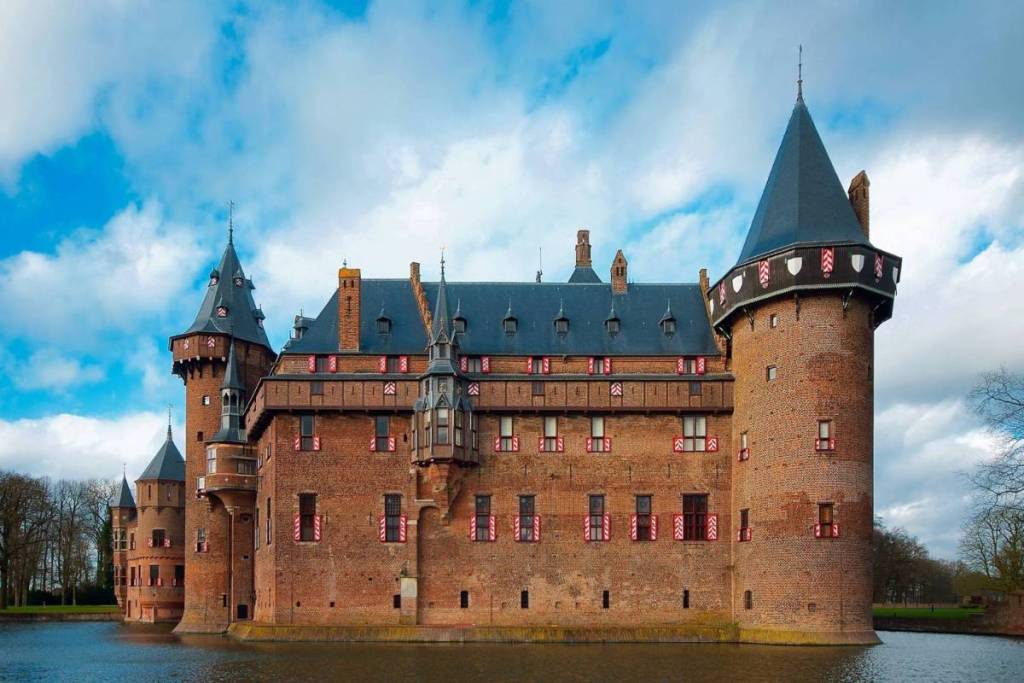 De monumentale bakstenen muren en neogotische torens van Kasteel de Haar met rood-witte vensterluiken aan het water.