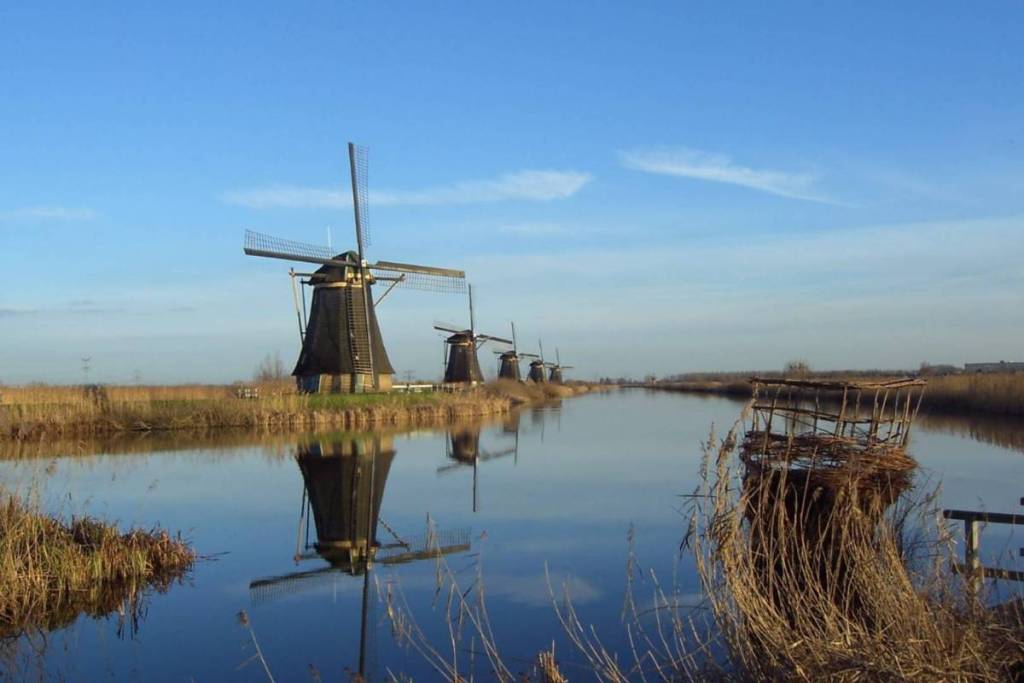 The iconic windmills of Kinderdijk reflected in the still waters of the polder beneath a clear blue sky.