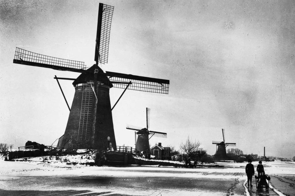 Historic black-and-white photo of the Kinderdijk windmills in a frozen winter landscape with children on the ice.