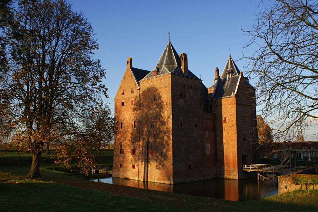 Vista del castillo medieval de Loevestein, con sus torres de ladrillo y su foso, bajo el sol del atardecer. Este castillo histórico de Gelderland es un lugar de interés cultural muy popular para pasar el día.