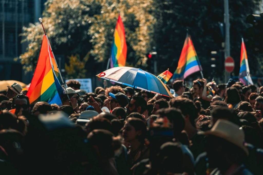 Gran multitud de fiesteros ondeando banderas arcoíris y con un paraguas arcoíris durante una fiesta callejera del WorldPride