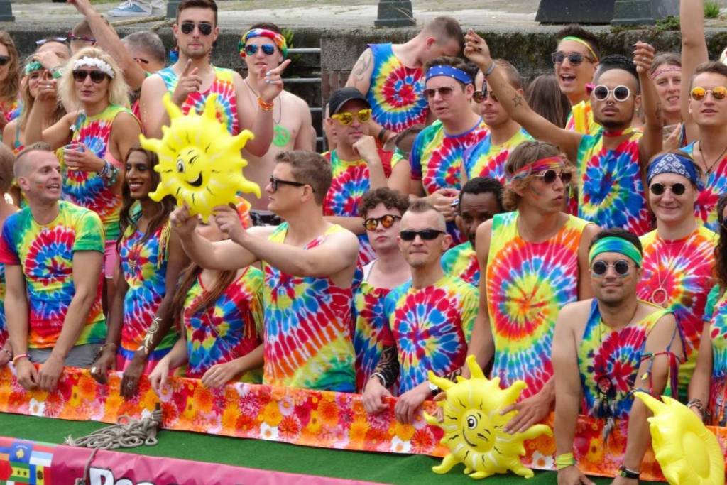 Un grupo de fiesteros con camisetas de tie-dye de colores y gafas de sol en un barco con tumbonas hinchables durante el WorldPride de Ámsterdam.