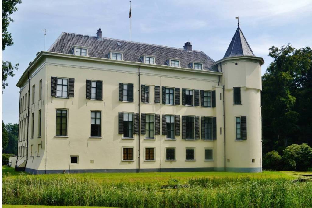 La storica villa Huis Doorn, con la sua facciata chiara, le persiane scure e la caratteristica torre angolare rotonda, affacciata su un canale verdeggiante.