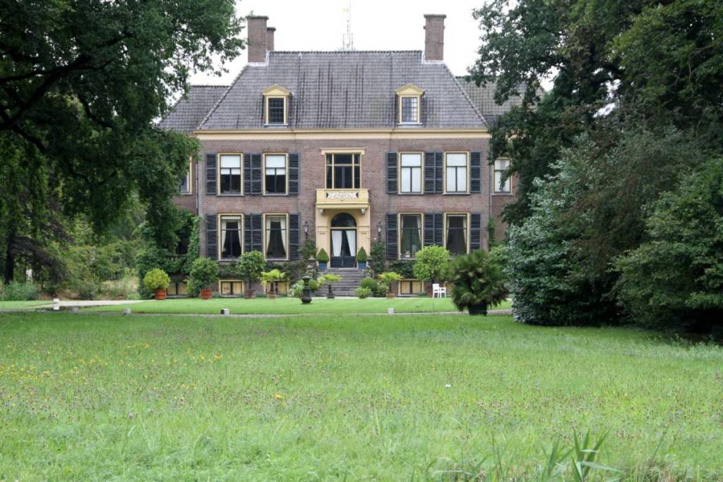 Vue de face de la maison de campagne en briques à Doorn, avec ses volets sombres, son perron et une pelouse verte sur le domaine.