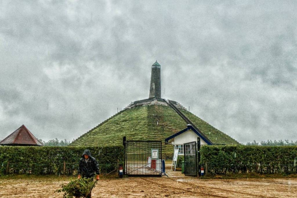 Een man loopt op een regenachtige dag met een kruiwagen voor de ingang van de Pyramide van Austerlitz in Woudenberg.