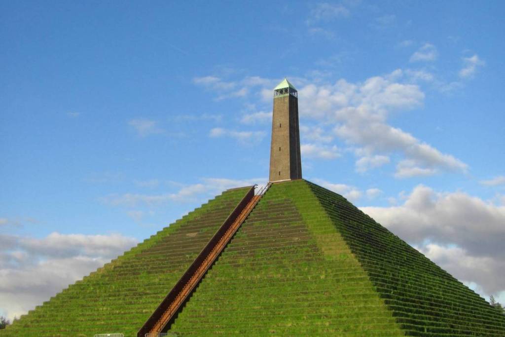 Vooraanzicht van de strak gemaaide Pyramide van Austerlitz met een lange houten trap naar de stenen obelisk op de top.
