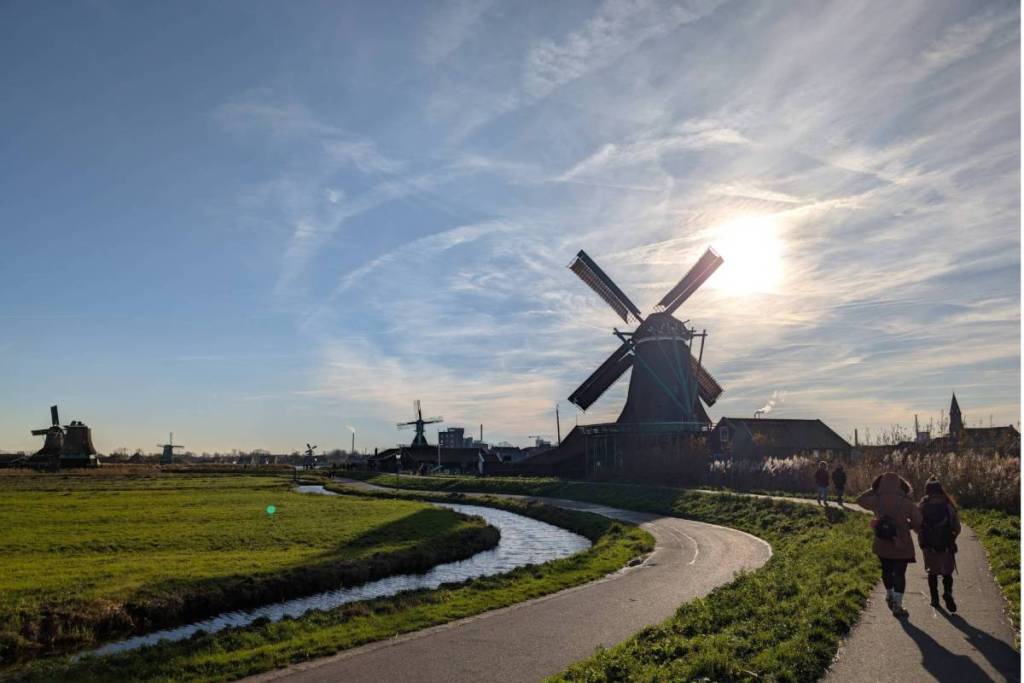 Sentiero lungo un canale del polder nel Kalverpolder con la sagoma di un mulino a torre in legno al tramonto allo Zaanse Schans.