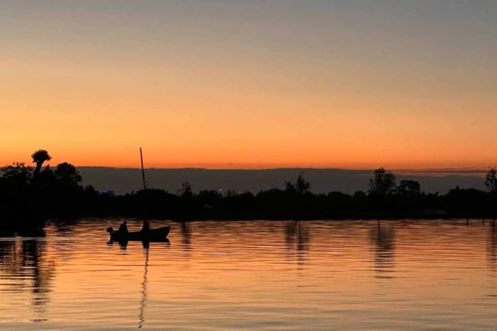 Silhouette d’un petit bateau sur l’eau lisse des Vinkeveense Plassen lors d’un coucher de soleil aux teintes orangées.