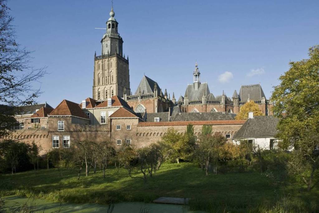 Zicht op de hoge kerktoren van de Sint-Walburgiskerk in Zutphen achter de historische stadsmuur.