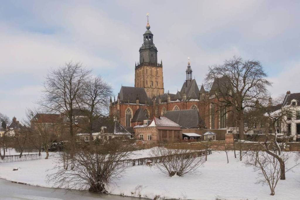 De Sint-Walburgiskerk in Zutphen in een besneeuwd winterlandschap met bevroren water op de voorgrond.