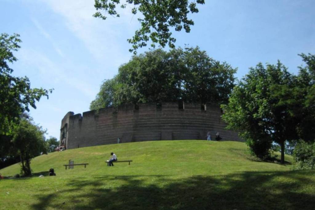 Vista lateral de la colina de motte de 12 metros de altura y la muralla de piedra del castillo de Leiden en un parque verde.