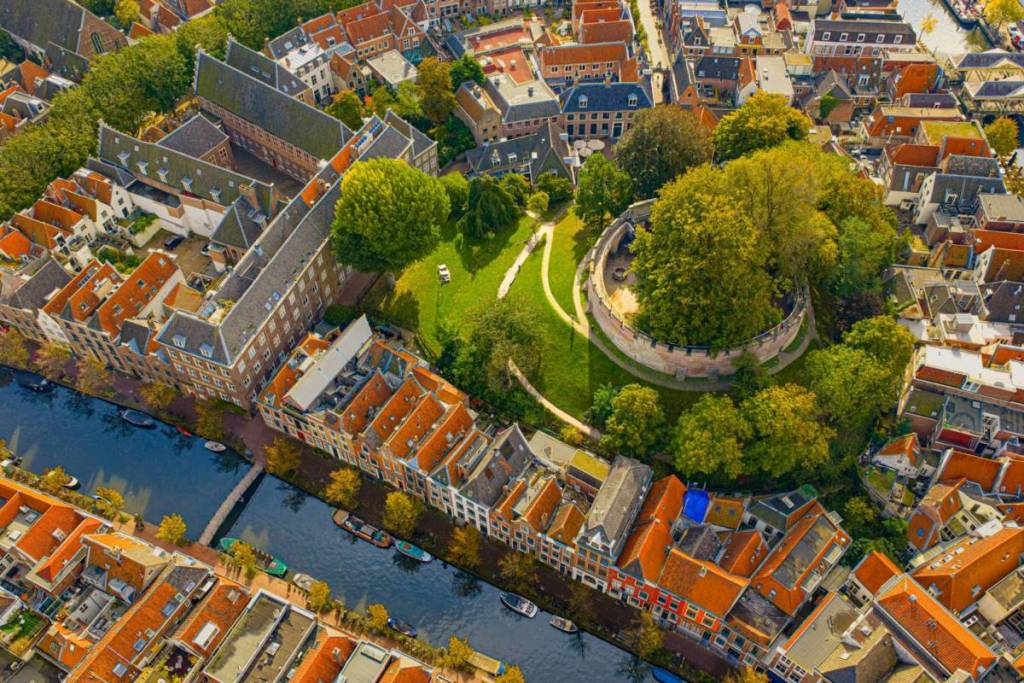 Foto aérea del castillo de motte circular «De Burcht» de Leiden, situado en la colina verde y rodeado de canales y tejados históricos.