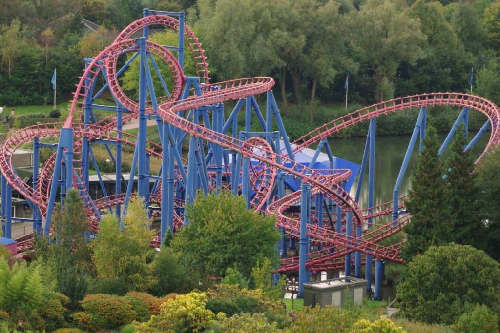 Übersicht über die Stahlachterbahn „Condor“ mit rosa Schienen und blauen Stützpfeilern über dem Wasser in Walibi Holland.