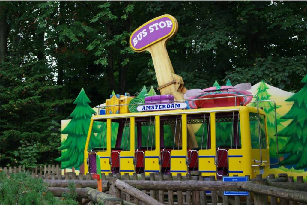 Farbenfrohe Kinderattraktion in Form eines gelben Busses mit der Aufschrift „Amsterdam“ im Familienpark von Walibi.