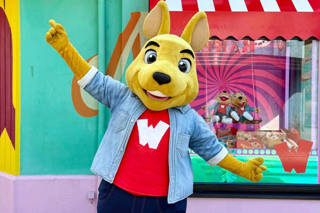 Das gelbe Känguru-Maskottchen von Walibi Holland in einer Jeansjacke heißt Familien in den Familienbereichen willkommen.