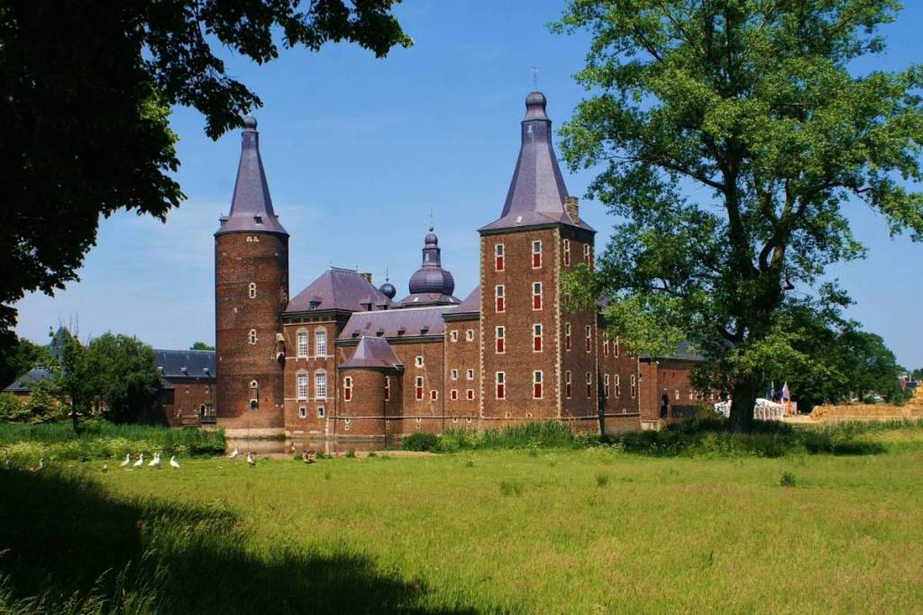 Una vista soleada del castillo medieval rodeado de agua, el castillo de Hoensbroek, en medio de árboles verdes y prados