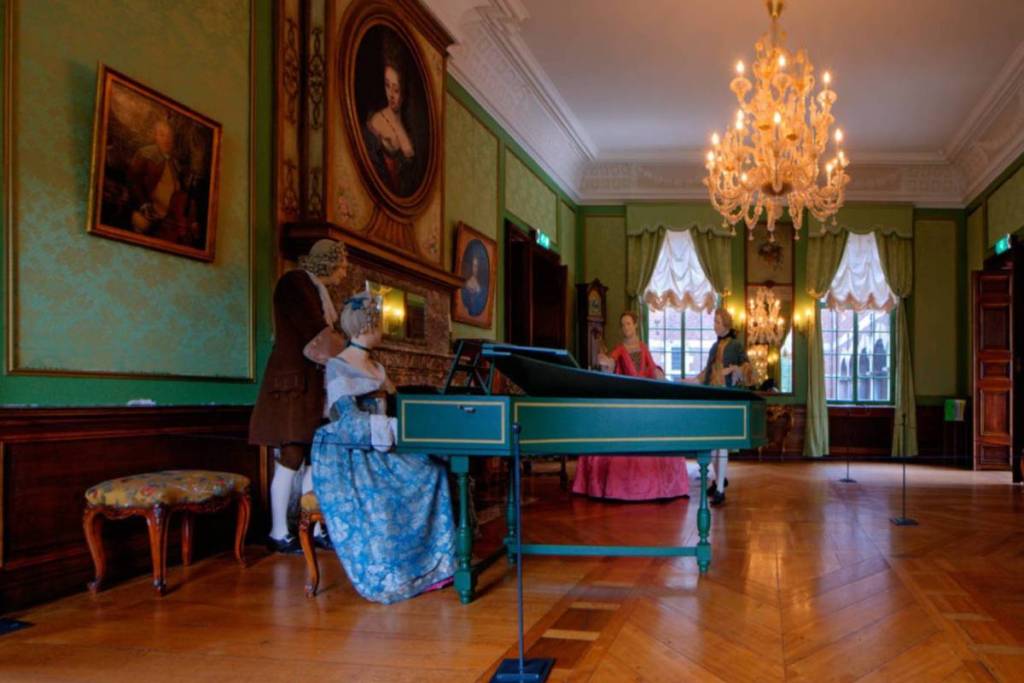 Salón de baile del siglo XVIII ricamente decorado en el castillo de Hoensbroek, con un clavicémbalo verde, una lámpara de araña de cristal y figuras con trajes de época