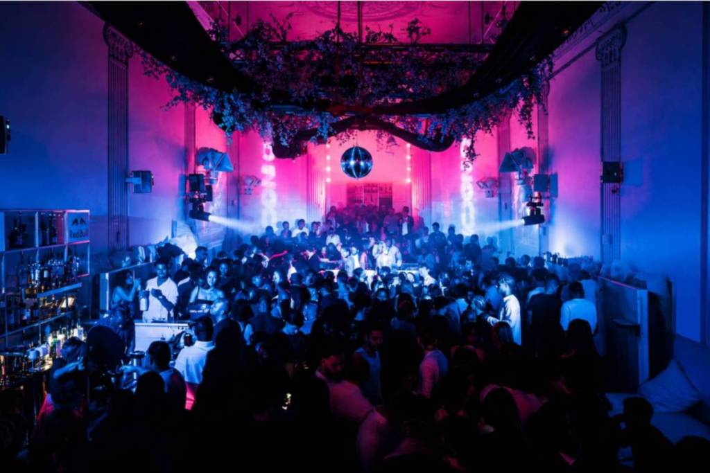 Vista general de la sala de baile del Supper Club de Ámsterdam, con luces de neón azules y rosas y una bola de discoteca.