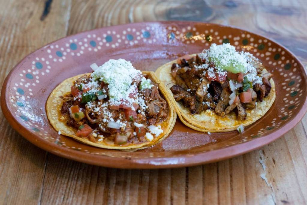 Two authentic Mexican tacos with tender meat, pico de gallo, and fresh cheese served on a terracotta dish in Amsterdam.