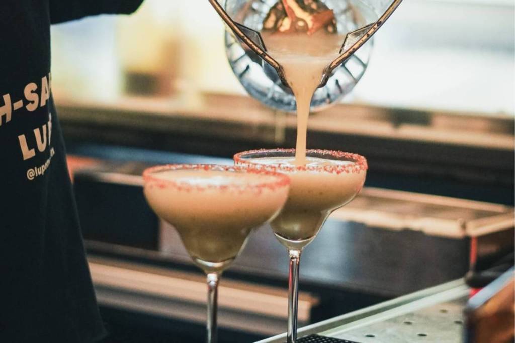 A bartender pouring fresh Mexican margaritas with a red chili salt rim at Lupe restaurant in Amsterdam.
