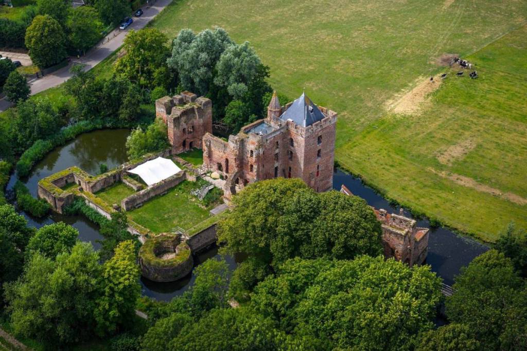 Foto aerea del Castello di Brederode, circondato da un fossato e da un fitto bosco verde, confinante con prati aperti.
