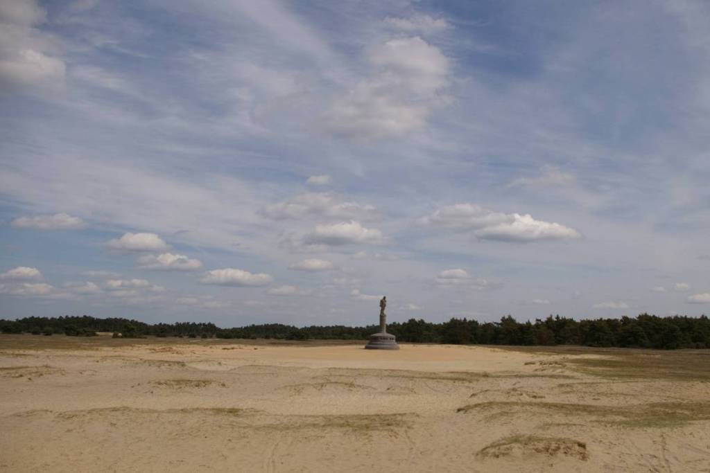 Vasta distesa di sabbia a De Hoge Veluwe con la statua del generale De Wet al centro, sotto un cielo leggermente nuvoloso.