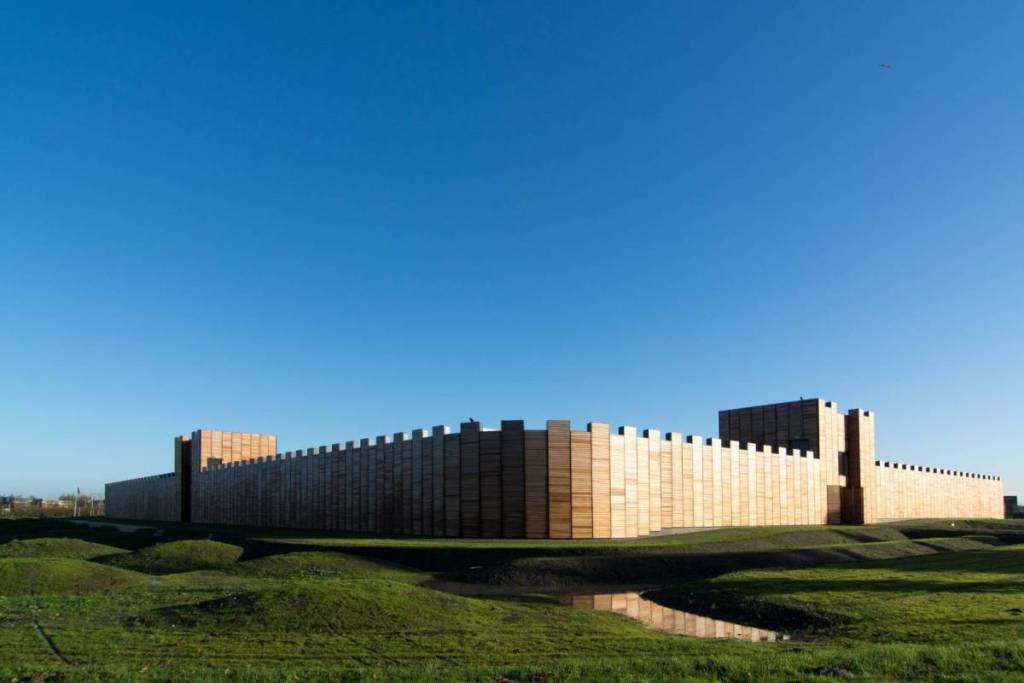Exterior view of the wooden fortification walls and ramparts of Castellum Hoge Woerd in Utrecht under a clear blue sky.