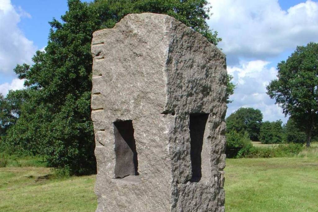 A large, rough stone monument with vertical recesses in a green grassland landscape on the Balloerveld.