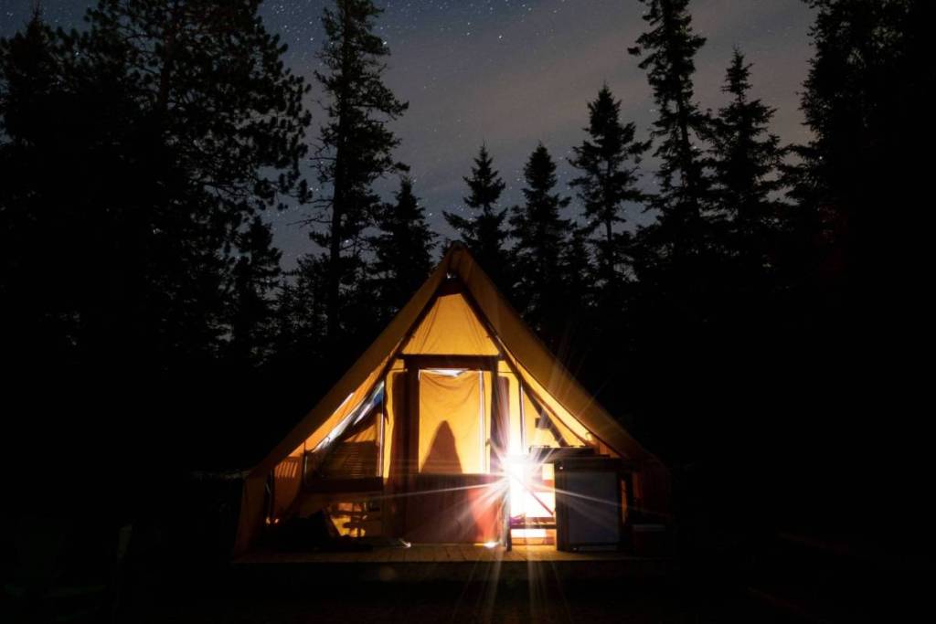 Sfeervol verlichte glampingtent op een natuurcamping in de bossen van de Veluwe onder een heldere sterrenhemel.