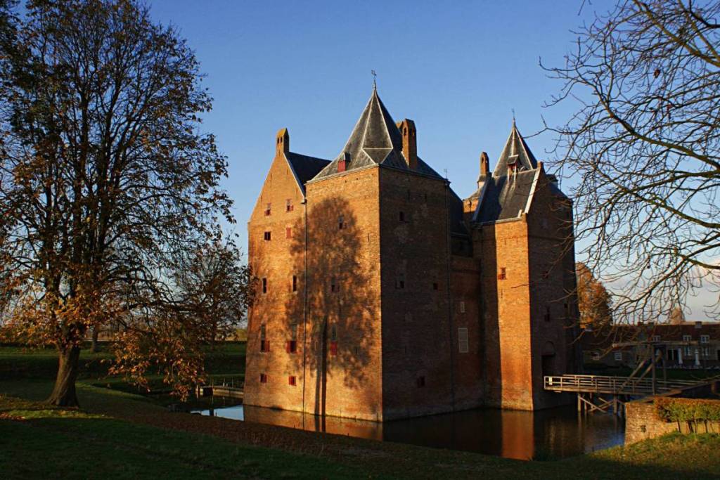 El castillo de Loevestein envuelto en la cálida luz dorada del atardecer, con las sombras de los árboles desnudos proyectadas sobre los viejos muros de ladrillo.