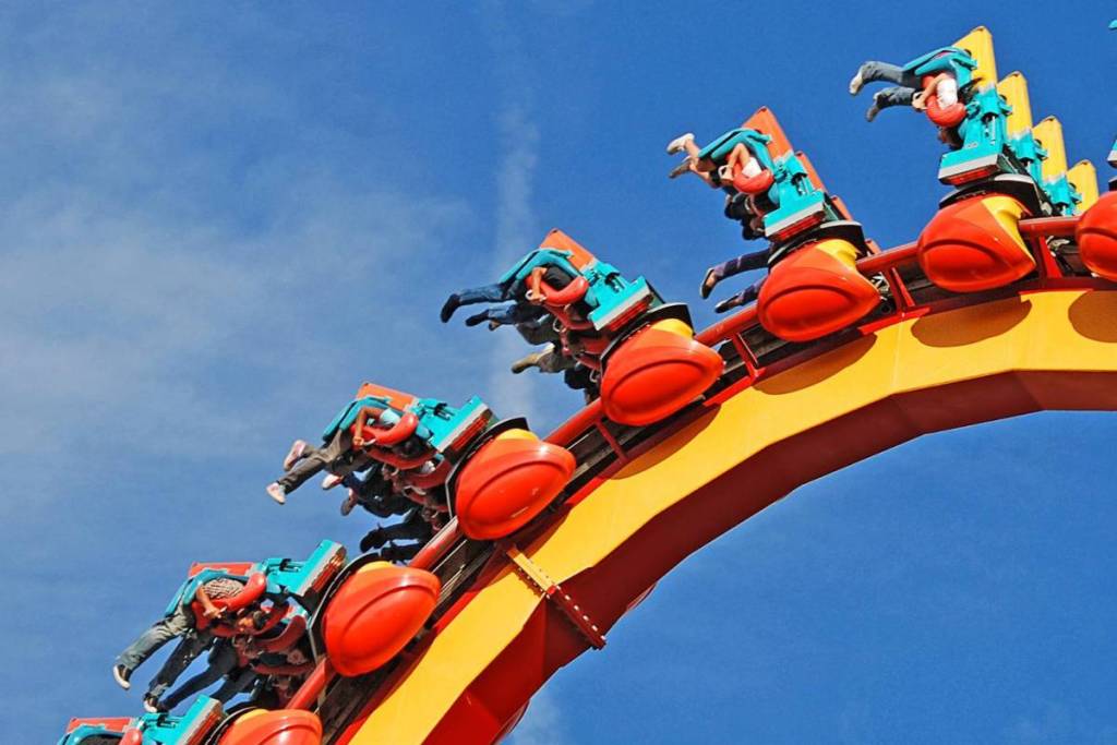 Visitantes en una montaña rusa amarilla y naranja en un bucle contra un cielo azul intenso en un parque de atracciones.