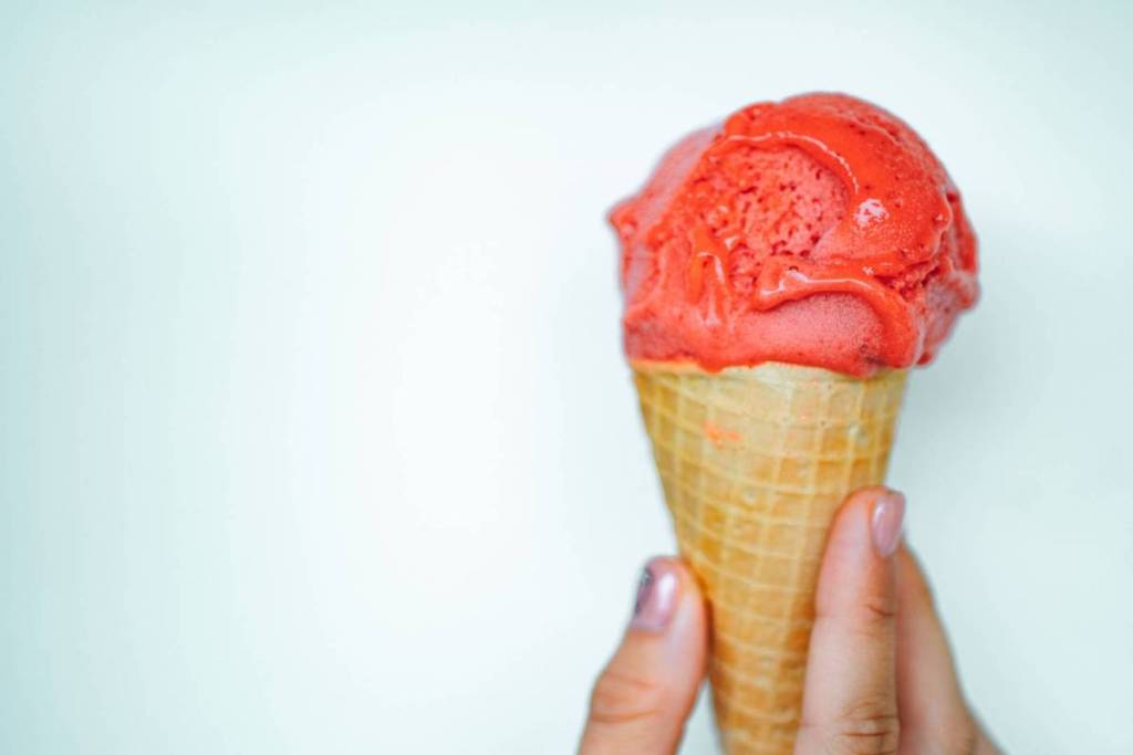 Mano que sostiene un cucurucho de barquillo con una bola de sorbete artesanal de frutos rojos.