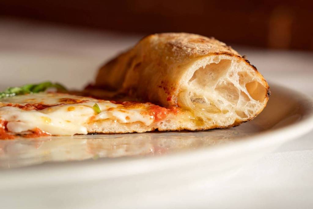 Close-up van een pizzapunt met gesmolten mozzarella, tomatensaus en een luchtige, knapperige korst.