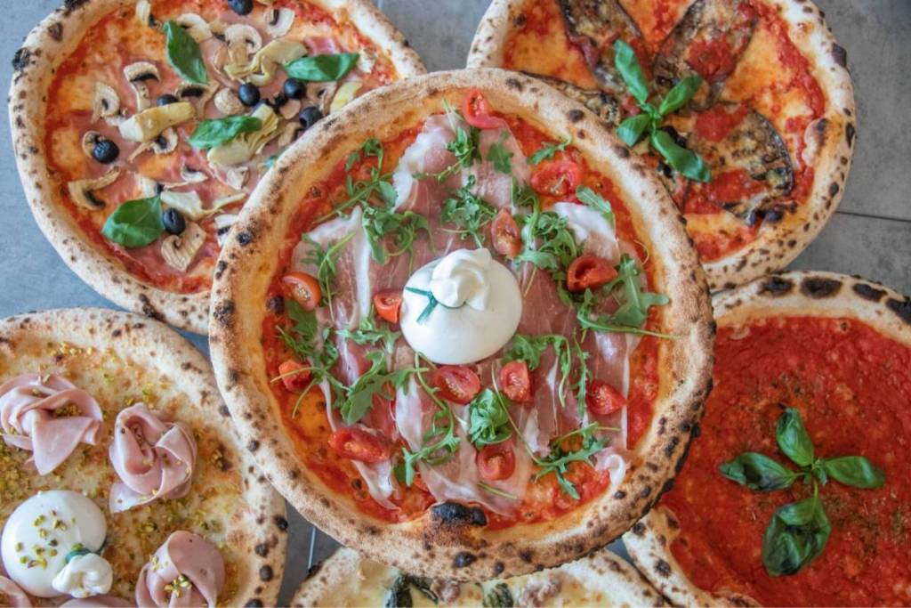 Bovenaanzicht van vijf verschillende ambachtelijke Napolitaanse pizza's met diverse toppings
