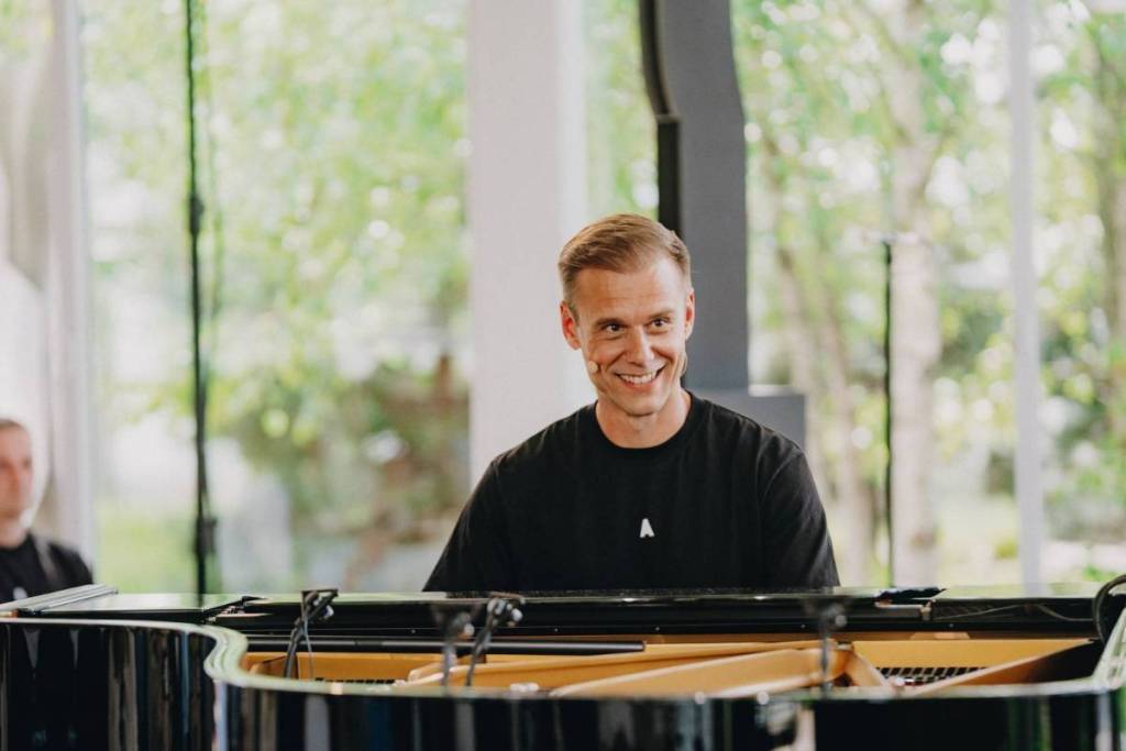 Primer plano de un Armin van Buuren sonriente detrás de un piano de cola durante un concierto íntimo.