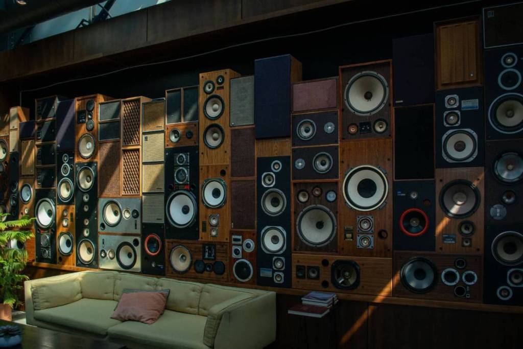 A wall completely covered with stacked vintage speakers above a sofa.