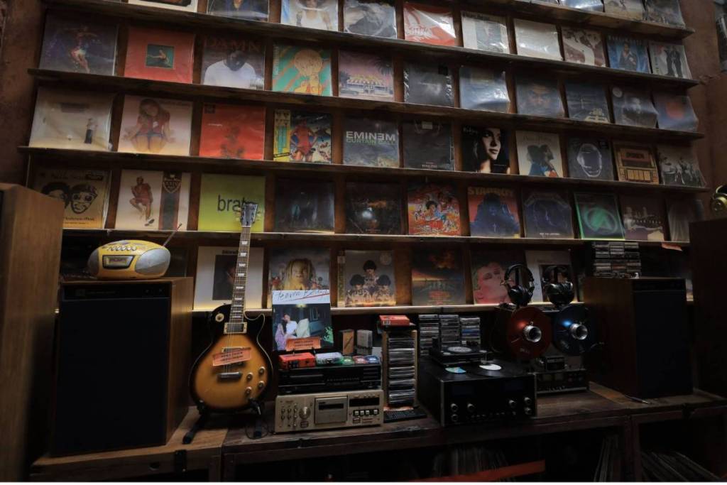 A wall full of LPs with retro audio equipment and an electric guitar in the foreground.