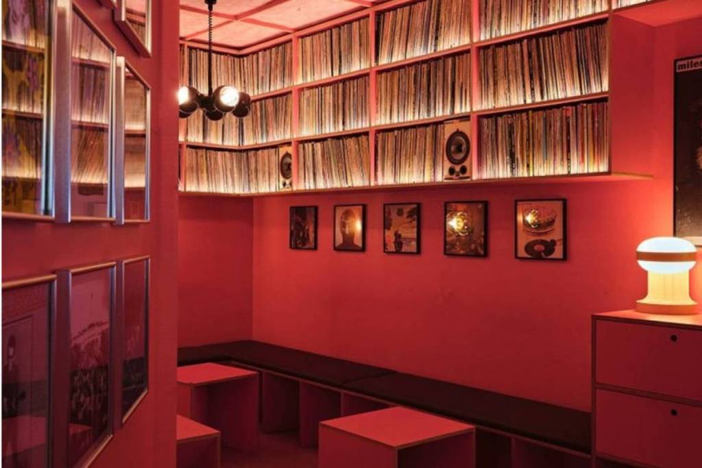 Corner of a red-lit hi-fi bar with record cabinets and framed LPs on the wall.