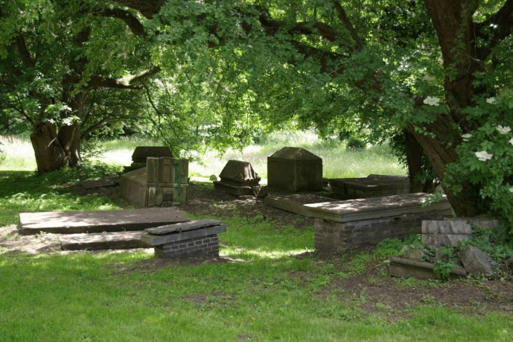 Zicht op de eeuwenoude, monumentale Joodse Begraafplaats Beth Haim in Ouderkerk aan de Amstel, met gevarieerde, historische grafstenen verscholen onder dichte boomkruinen.