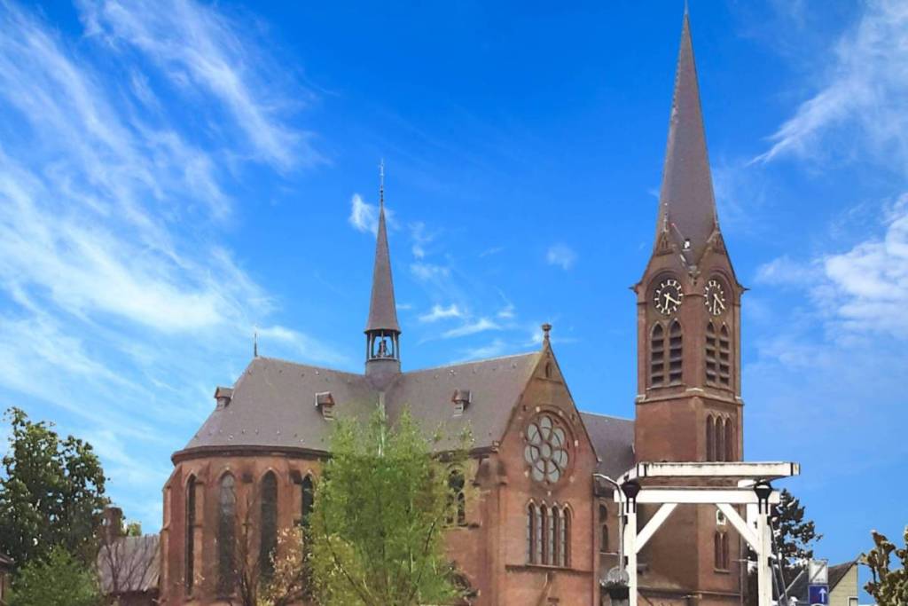 Zij-aanzicht van de neogotische St. Urbanuskerk in Ouderkerk aan de Amstel met een typisch witte Hollandse ophaalbrug op de voorgrond onder een blauwe lucht.