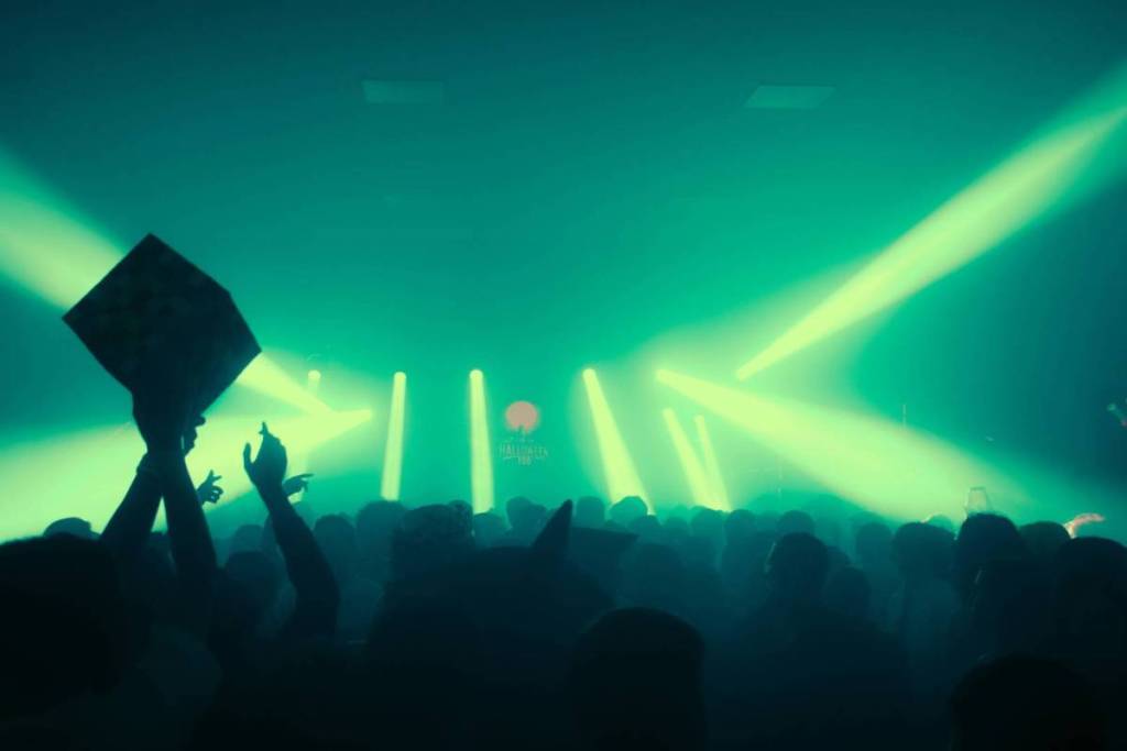 Feestvierende menigte in een club, gehuld in felle groene laserstralen vanaf het podium.
